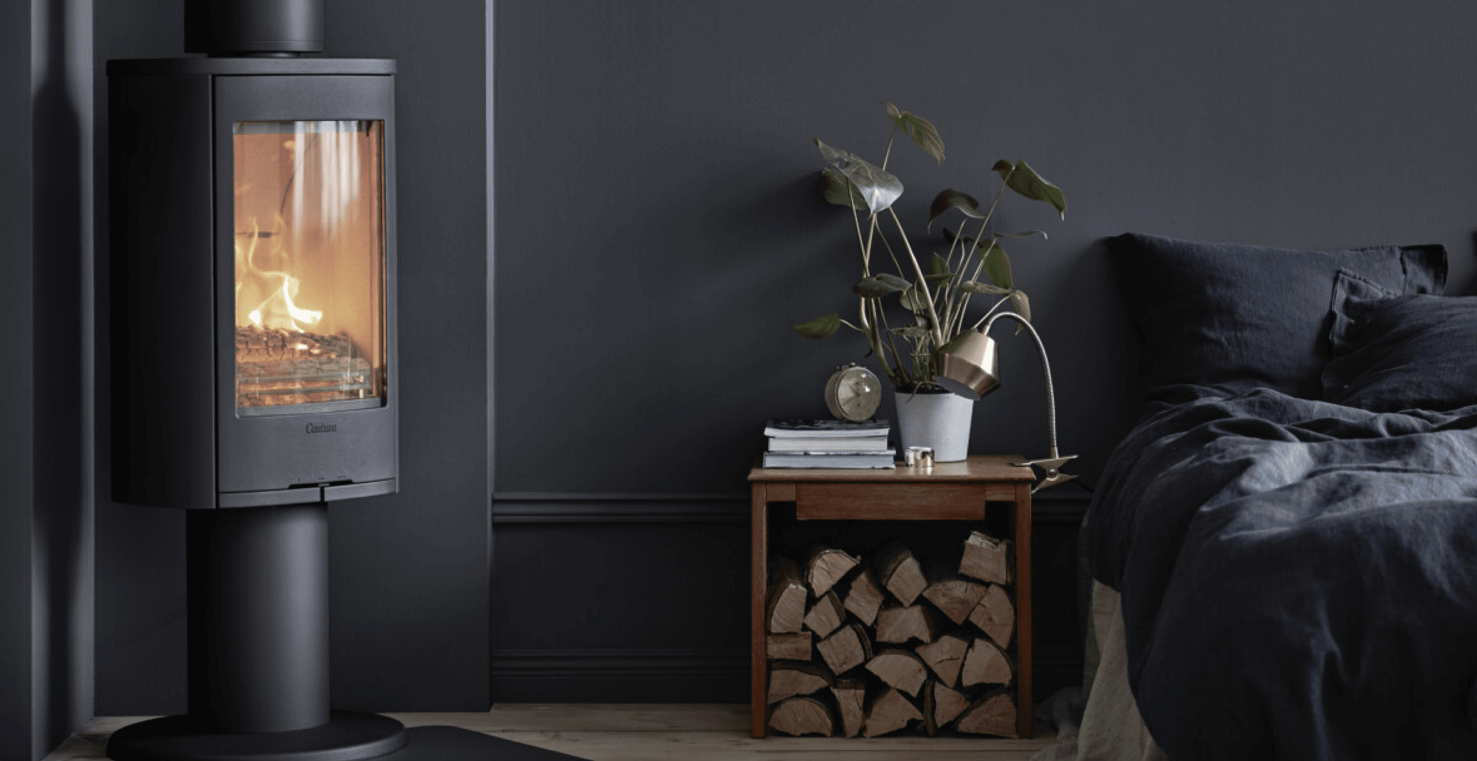 A Contura wood-burning stove lit in a dark, styled bedroom interior